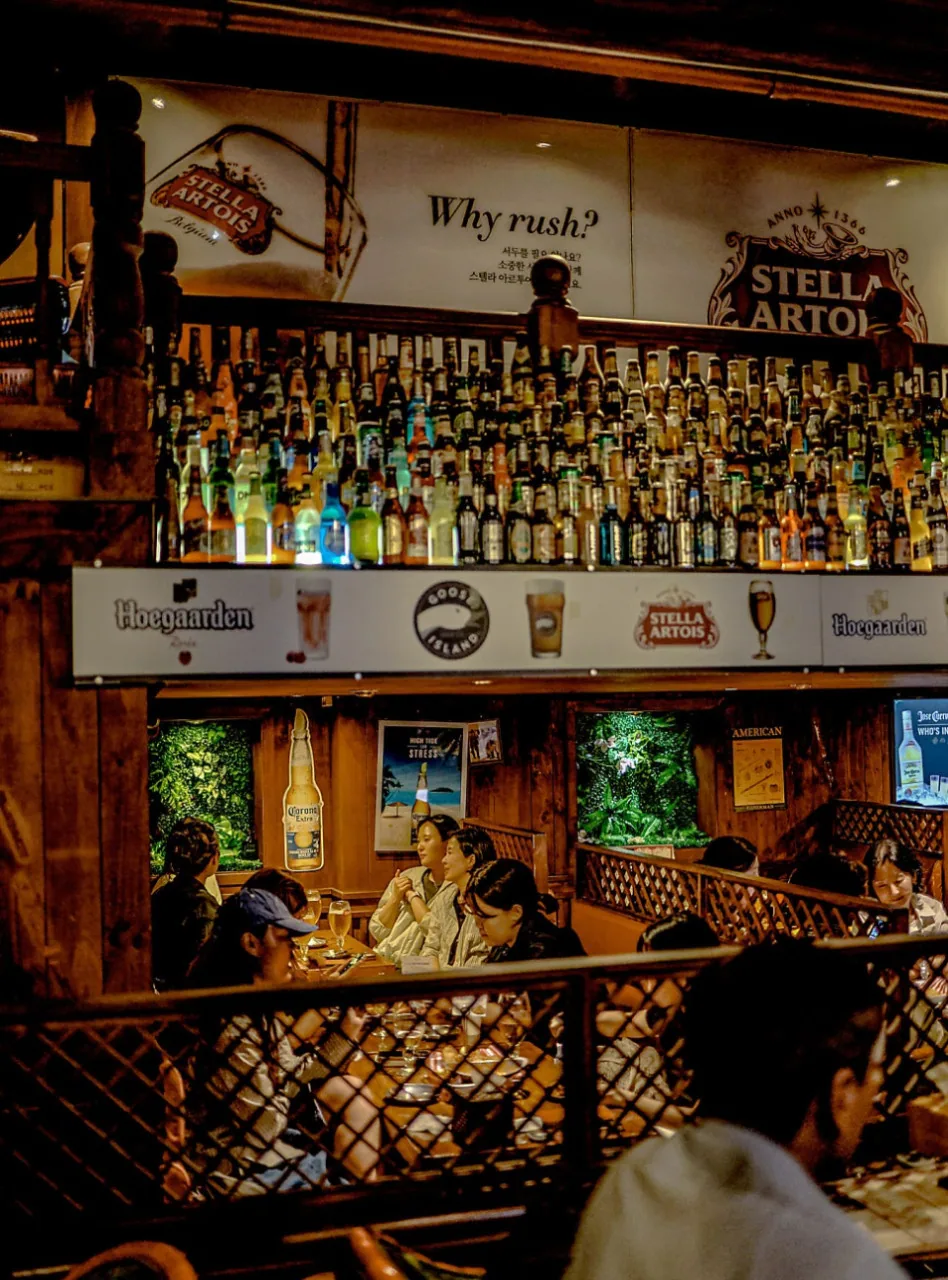 JH Texas Bar interior — hundreds of beer bottles lining the wall, Stella Artois "Why rush?"